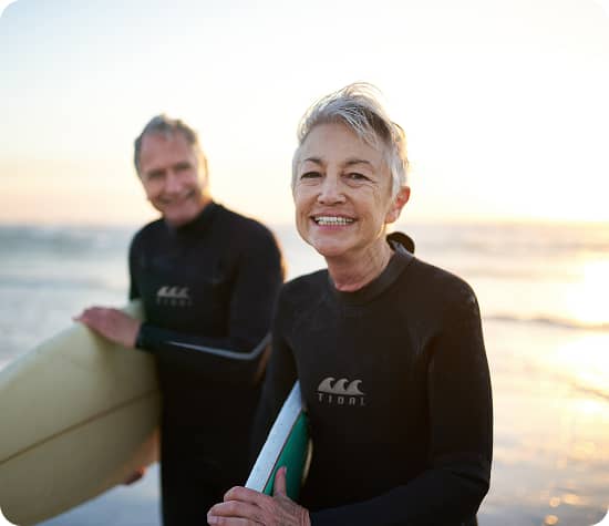 Two people in wetsuits, holding surfboards and smiling at the camera