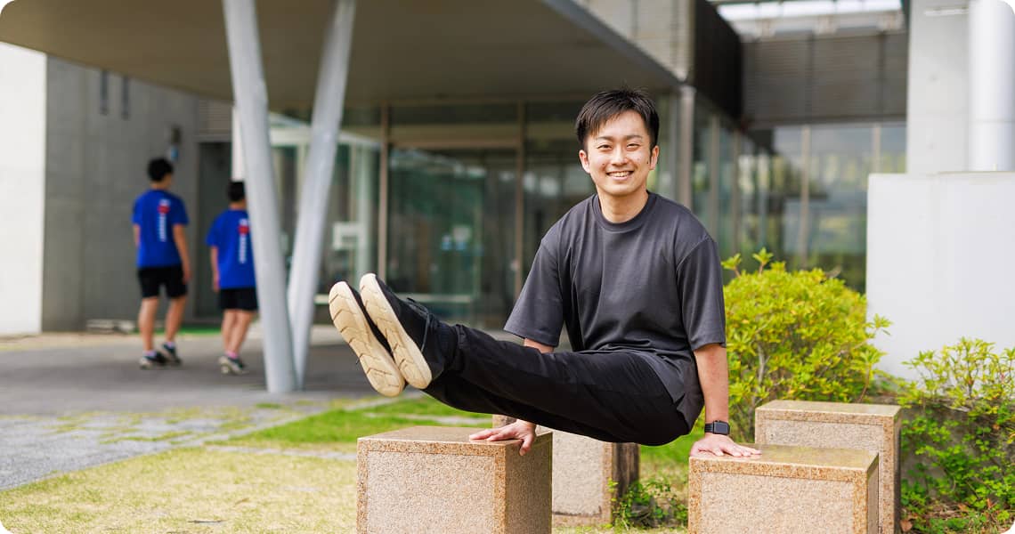 Person smiling and holding an L sit outside