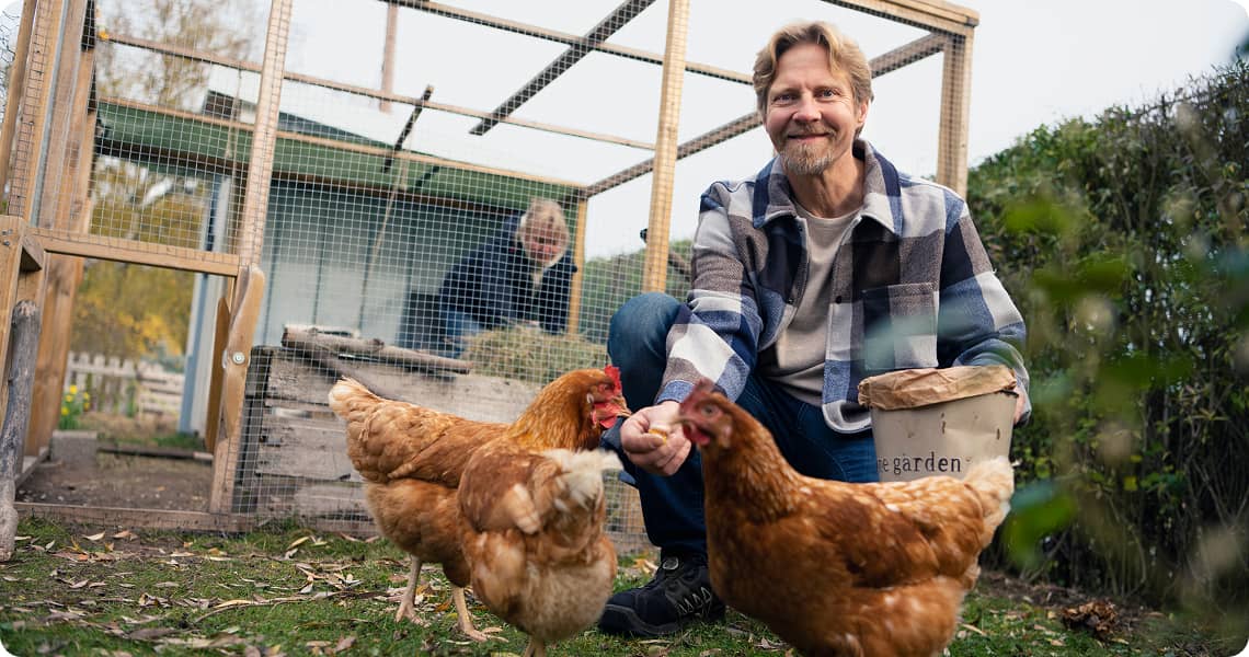 Person smiling and feeding chickens outside of a coop