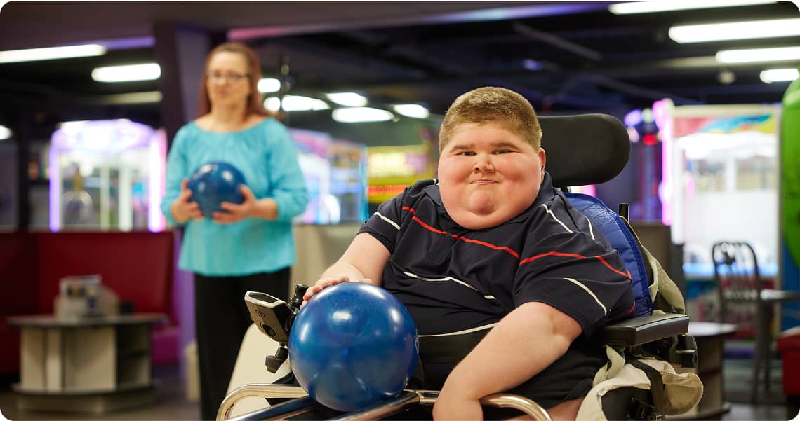 Child in a wheelchair bowling and grinning at the camera